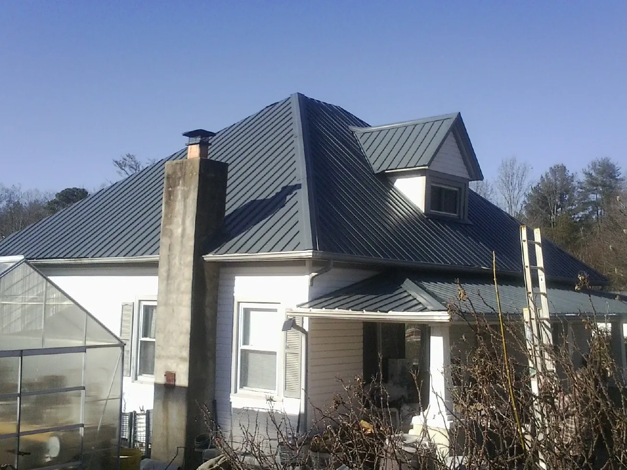 Dark blue standing seam metal roof on a white farmhouse with dormer — Slate & Tile Roof Repair by Roofing Brothers in Mc Leansville