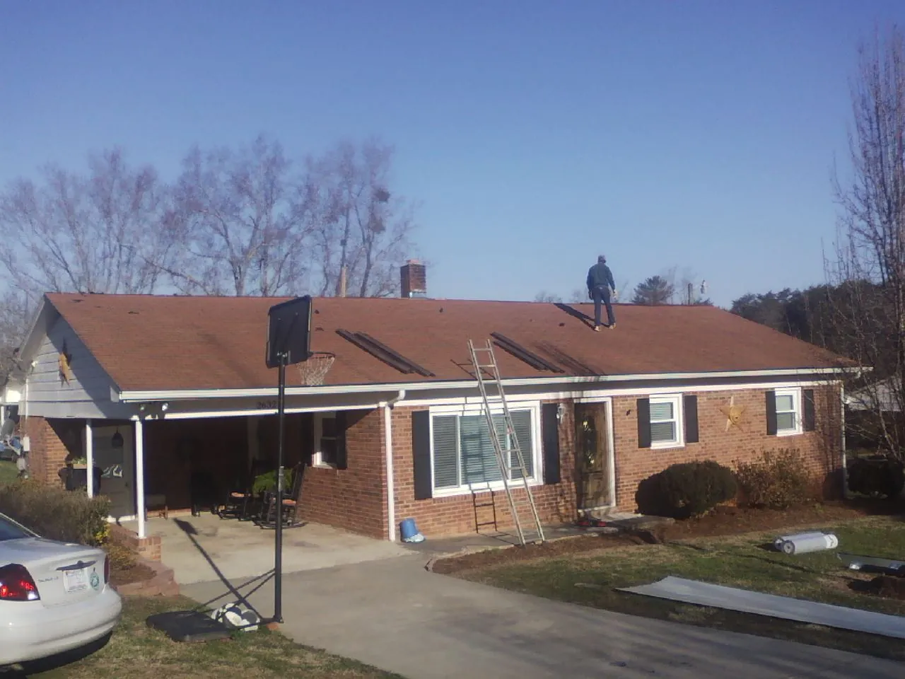 Roofer stripping a shingle roof on a brick ranch before metal panels in Mc Leansville