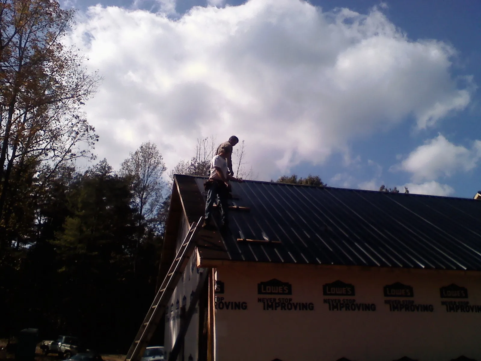 Roofer fastening dark metal panels high against a cloudy sky, from a Roof Inspection job in Mc Leansville