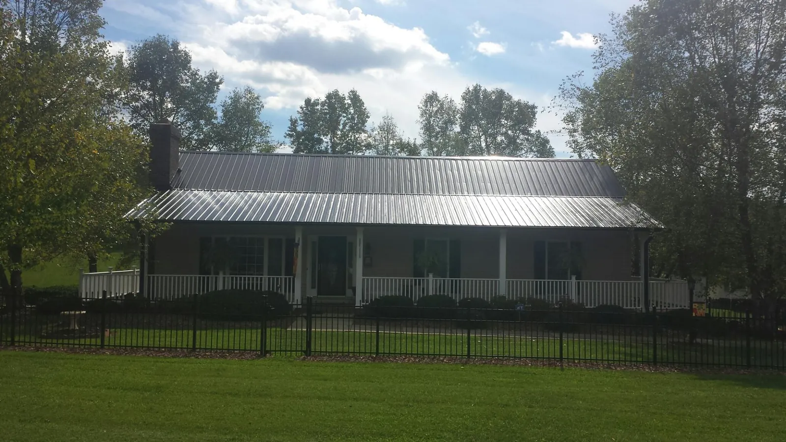 Gray metal roof on a brick ranch with a full width front porch — Gutter Guard Installation work by our crew in Mc Leansville