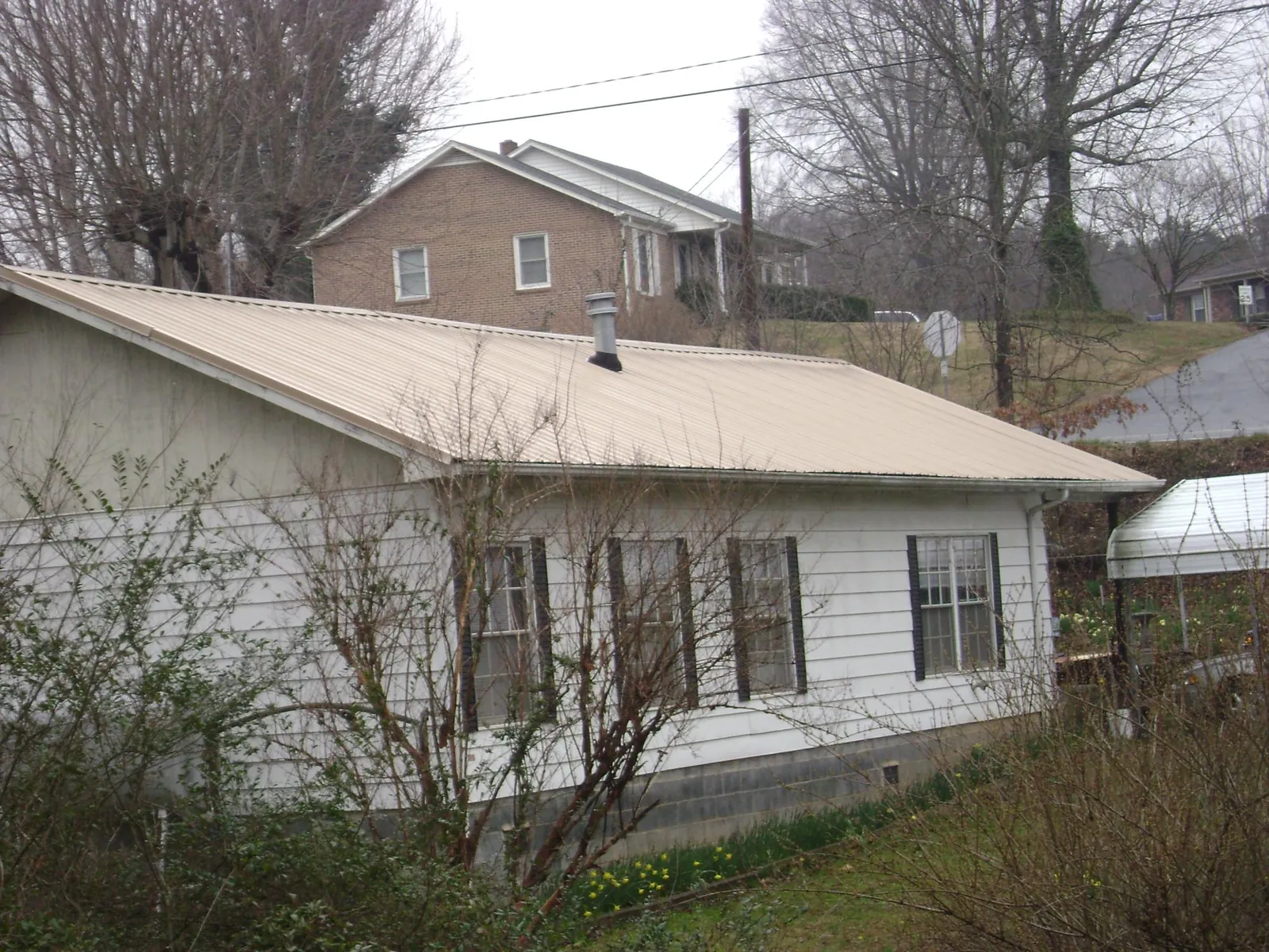Tan metal roof on a white sided house set into a hillside — Commercial Roofing by Roofing Brothers in Mc Leansville